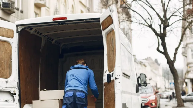 Repartidor cargando cajas en una camioneta de reparto estacionada en una calle de la ciudad.