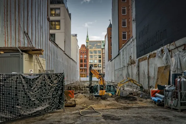 Excavadoras trabajando en una obra de construcción urbana entre edificios y vallas perimetrales.