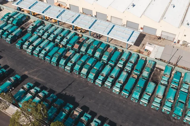 Vista aérea de un patio logístico con decenas de camiones estacionados en filas junto a una bodega.